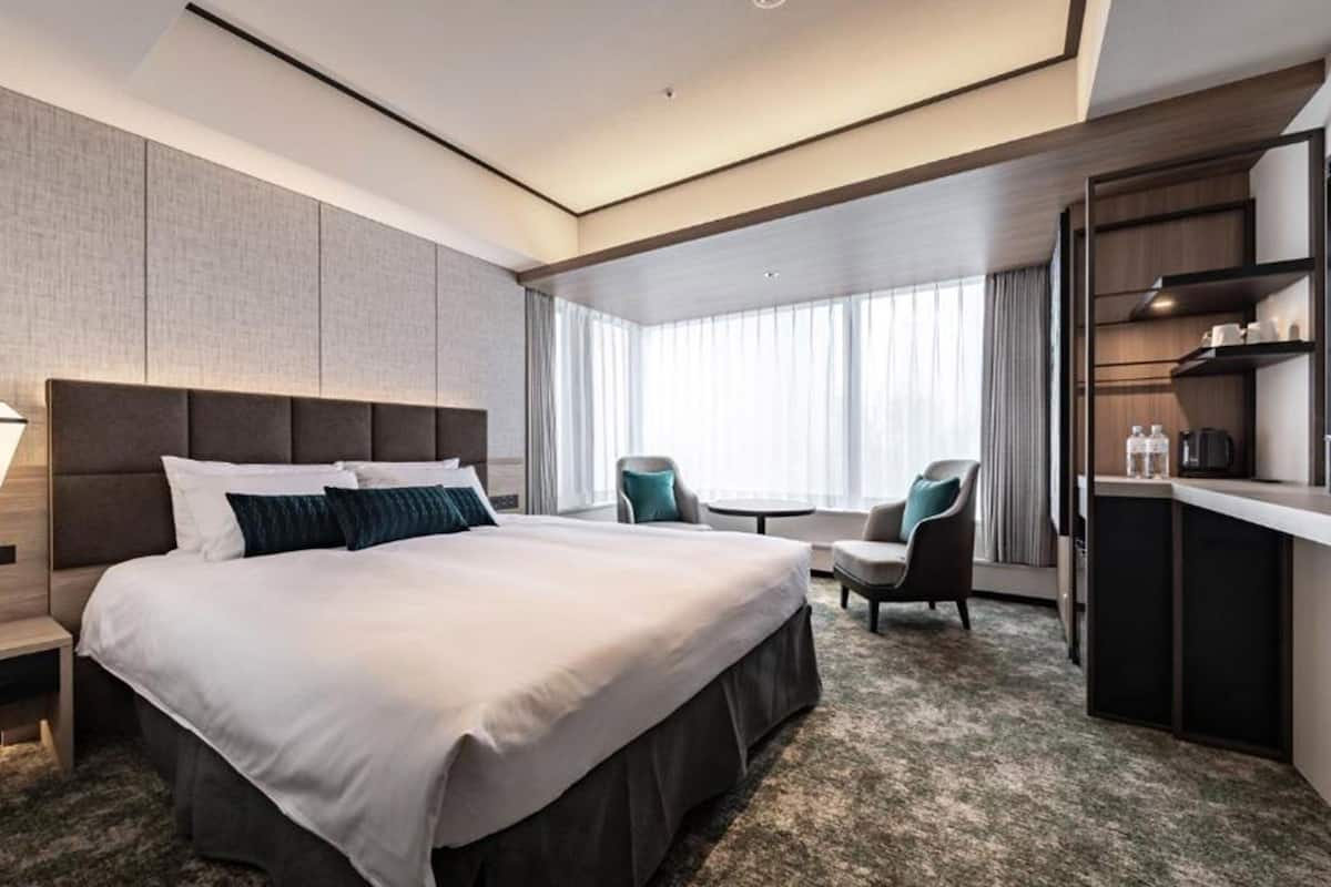A modern hotel room with a large bed, a desk, and a chair.