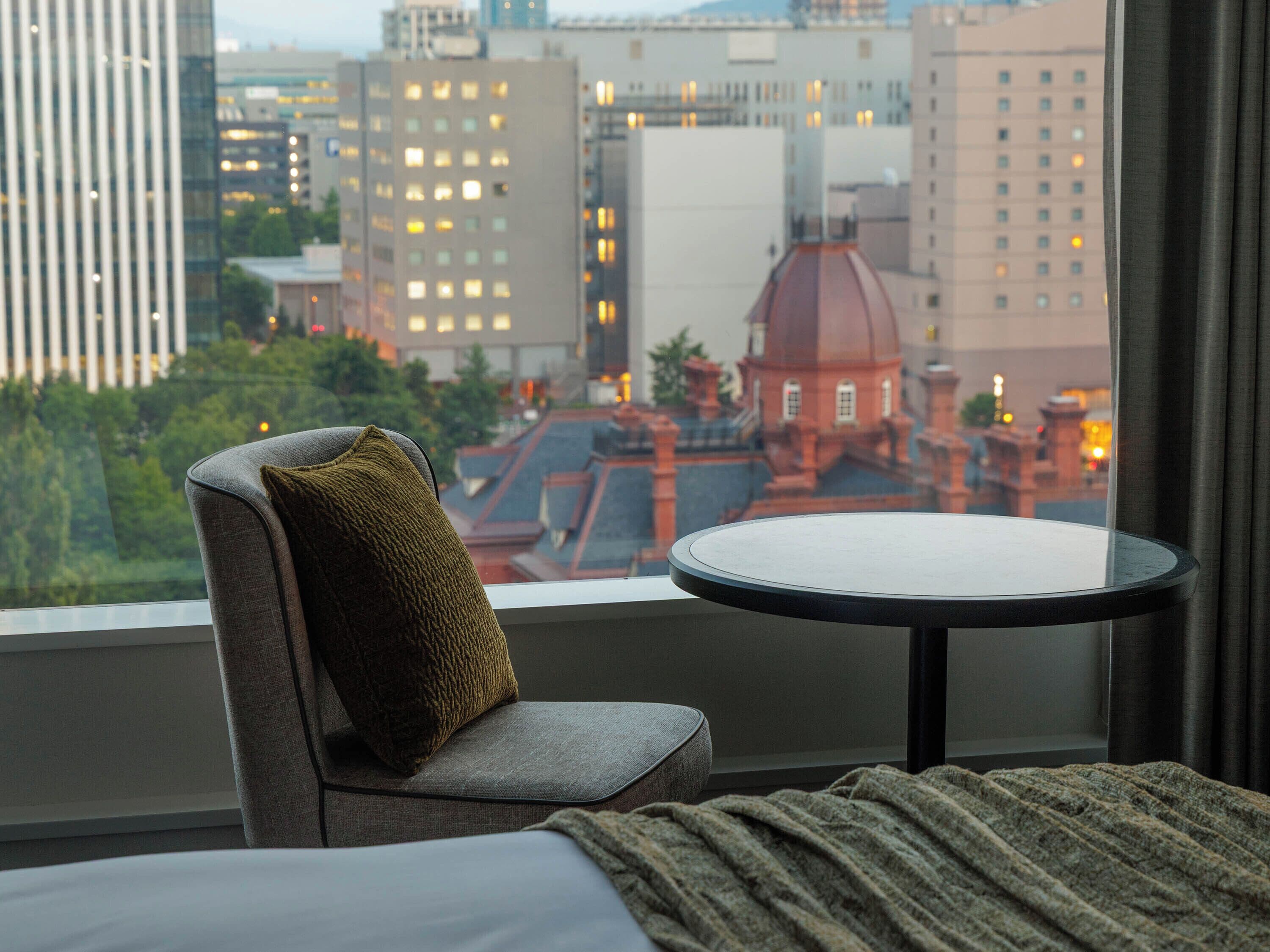 Une chambre d’hôtel avec vue sur la ville, une table ronde, une chaise avec un coussin et un lit.