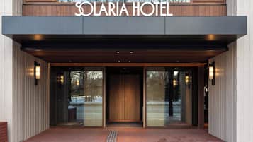 La entrada del Hotel Solaria con un diseño moderno, destacando un amplio acceso de madera, puertas de cristal y un camino de ladrillo que conduce a la entrada.