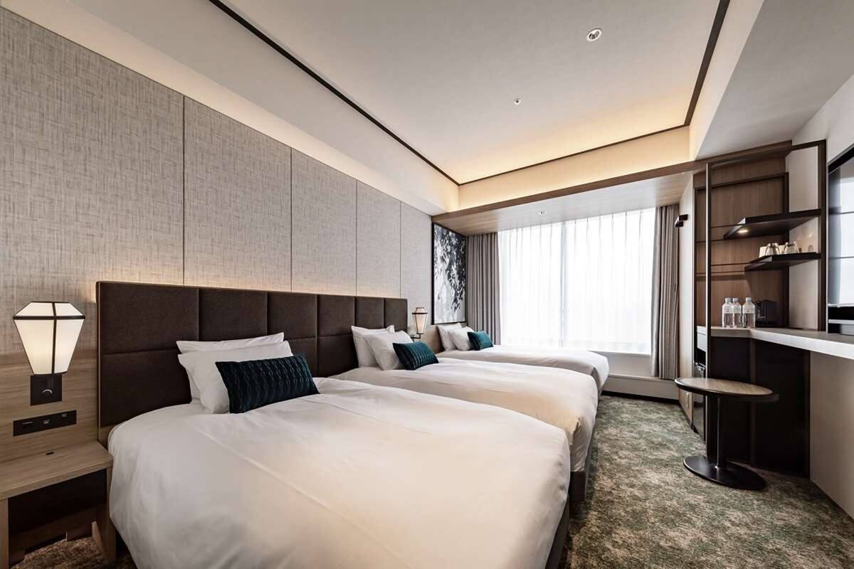 A hotel room with two beds, a desk, a chair, a lamp, and a large window.