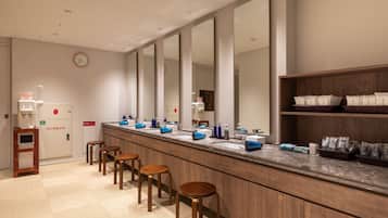 A modern bathroom with a long counter, multiple mirrors, and wooden stools.