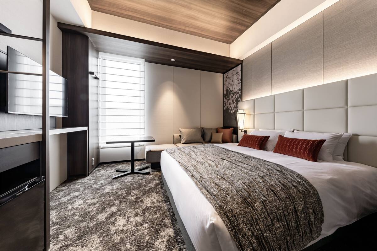 A modern hotel room with a large bed, a desk, and a built-in TV.