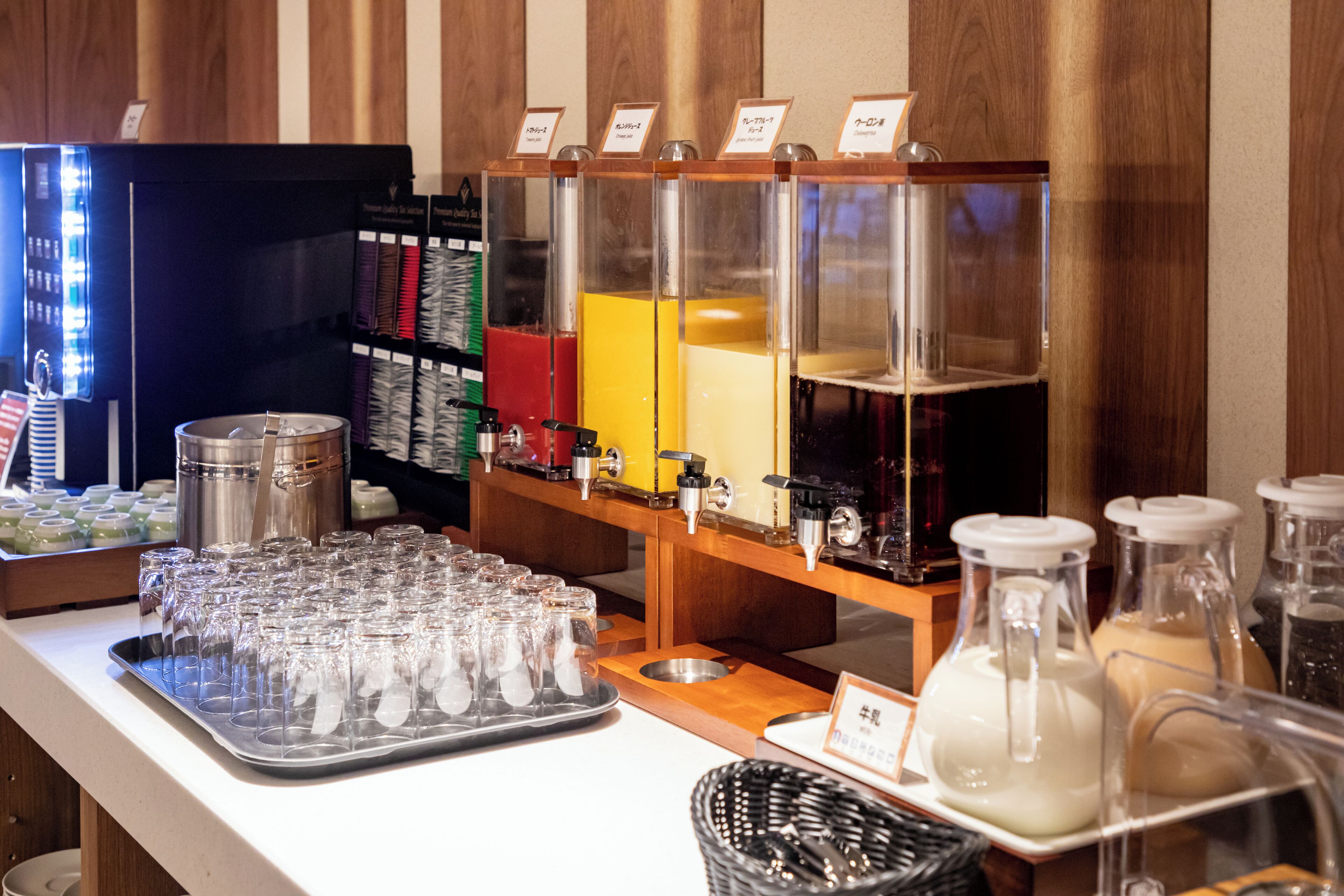 A buffet setup with various food containers and a tray of glasses.