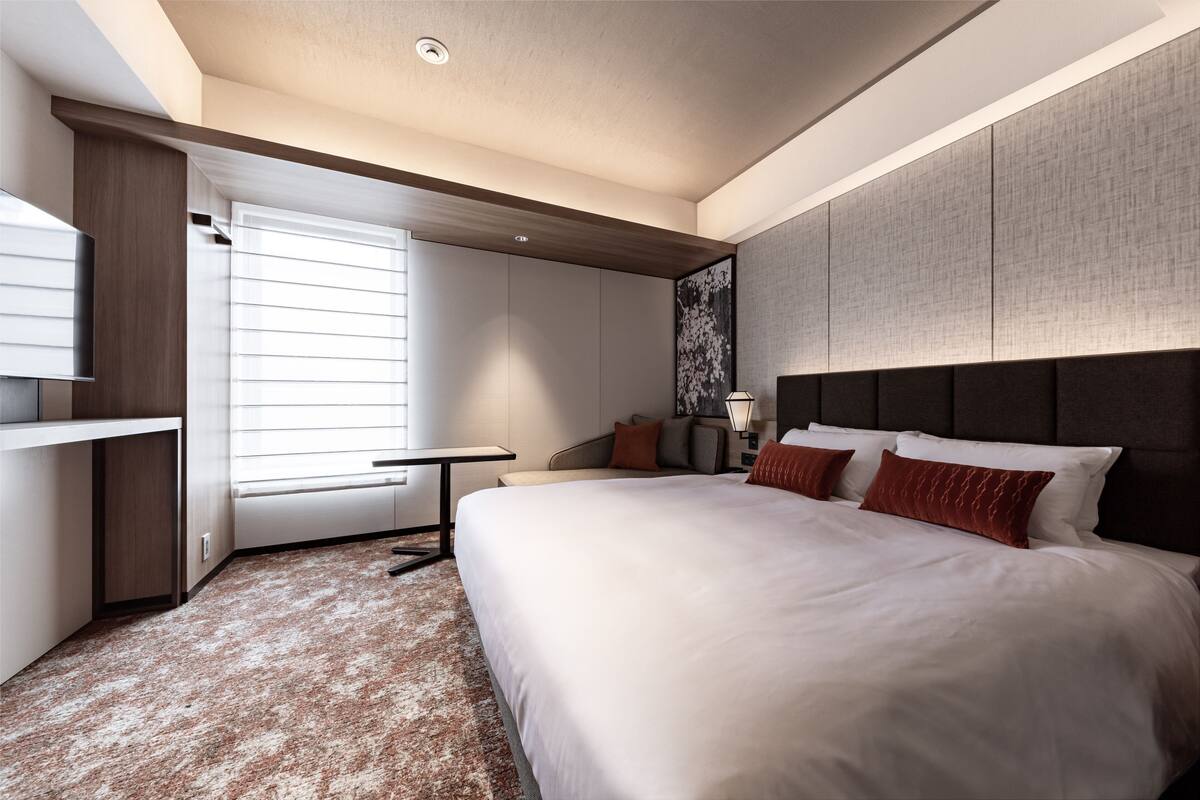 A modern hotel room with a large bed, a desk, a chair, and a TV.