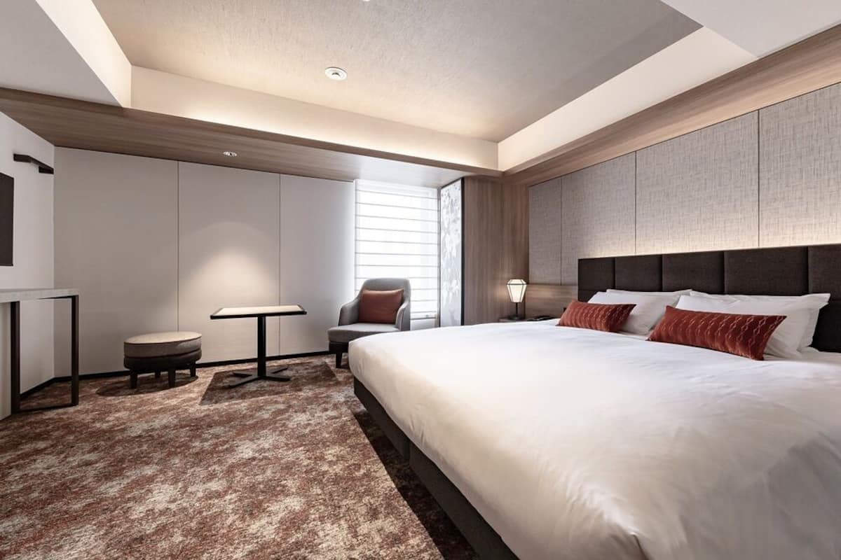 A modern hotel room with a large bed, a desk, a chair, and a small table.