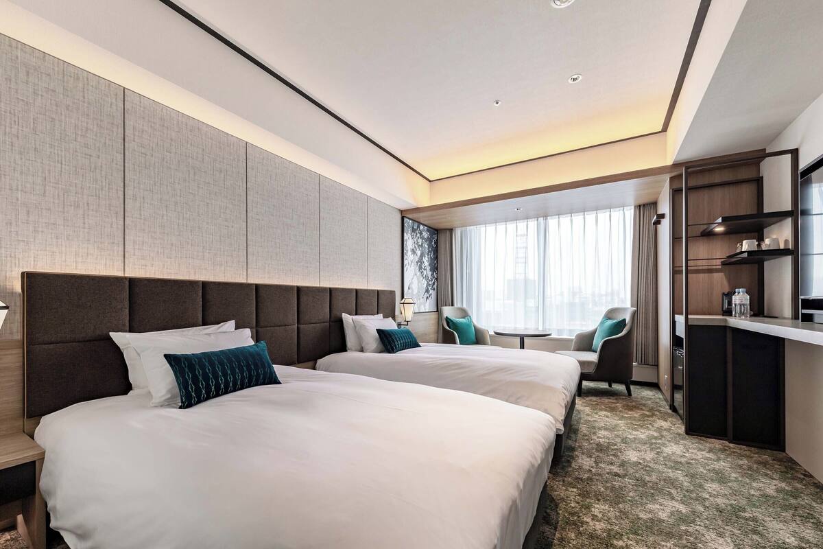 A modern hotel room with two large beds, a desk, and a seating area.