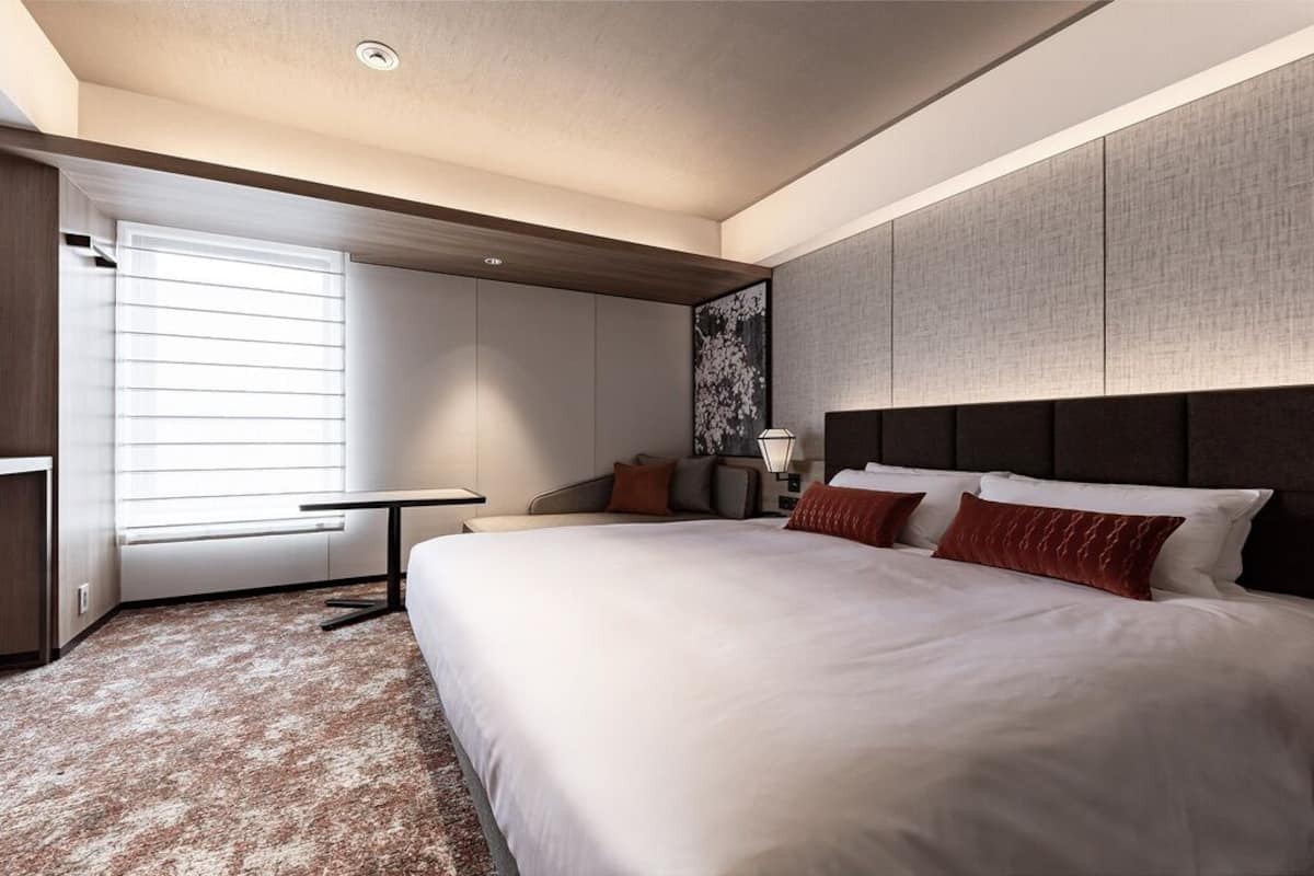 Ein modernes Hotelzimmer mit einem großen Bett, einem Schreibtisch und einem Fenster mit Jalousien.