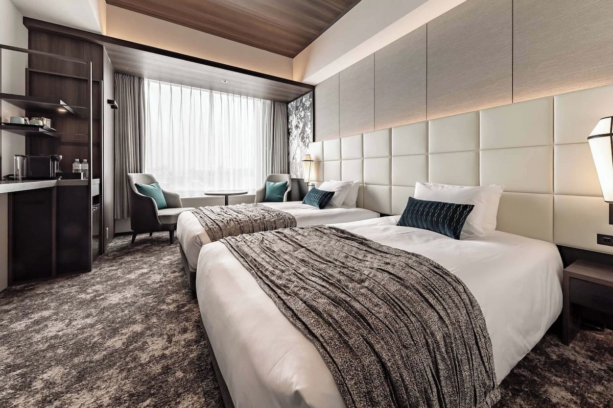 A hotel room with two beds, a desk, and a seating area.