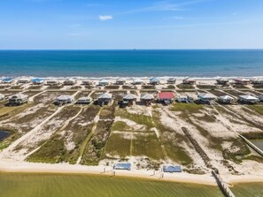 Luchtbeeld van een kustgebied met woonhuizen op palen, een strand en een heldere lucht.