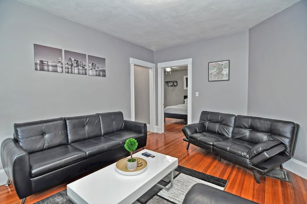 A modern living room with two black leather sofas, a white coffee table, and a small potted plant.