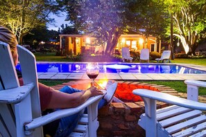 A person relaxing by a poolside with a glass of wine, surrounded by outdoor seating and a well-lit patio area. - Biweda Nguni B&B (Jozini)