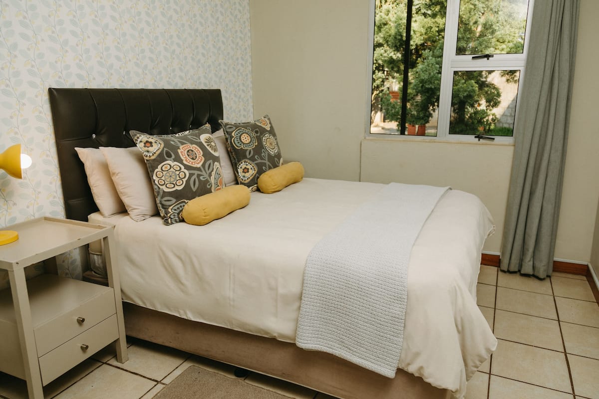 A bedroom with a bed, bedside table, and a window with a view of trees.