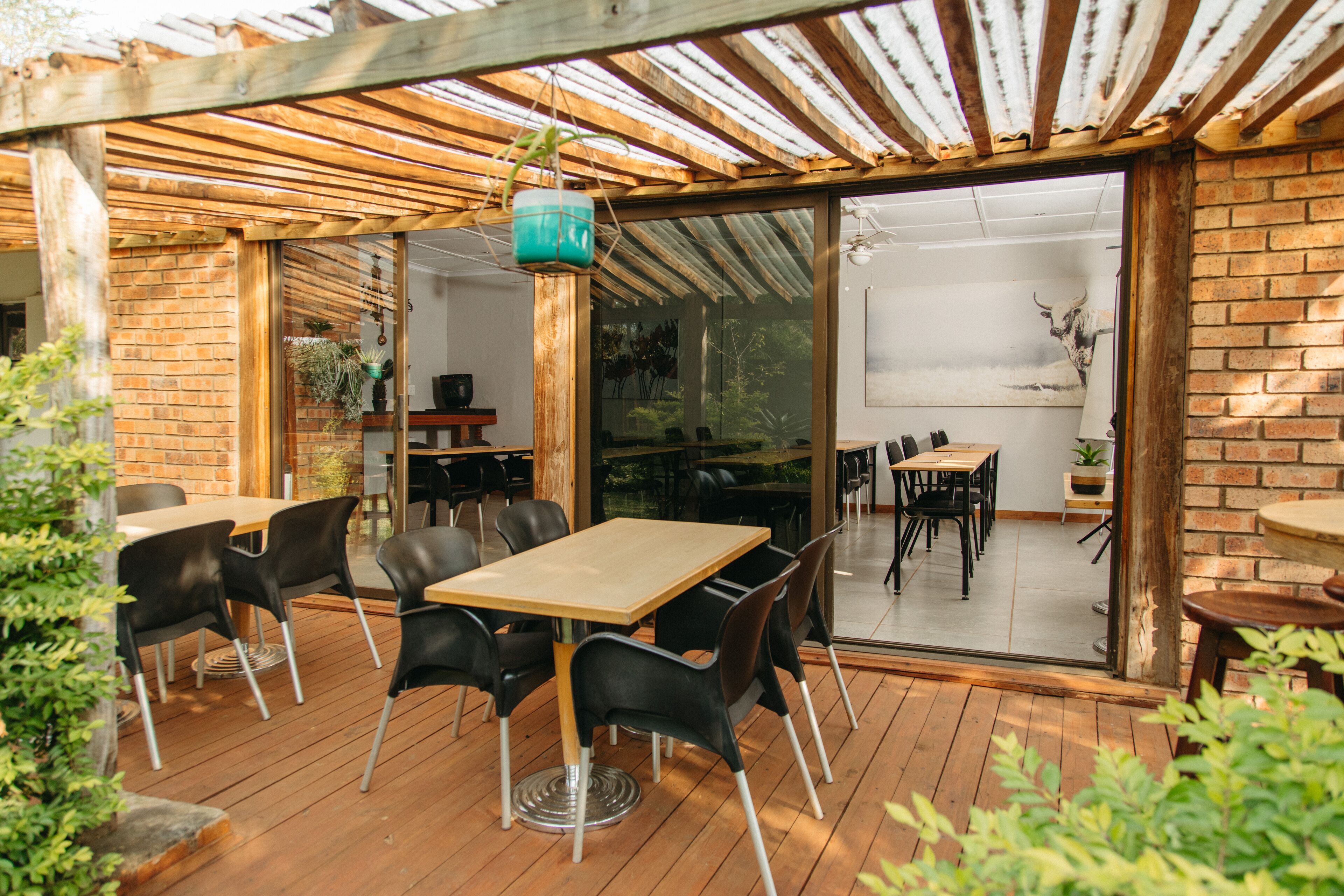 Un patio exterior con suelo de madera, sillas negras y una mesa de madera.