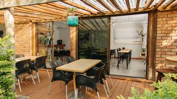 Un patio exterior con suelo de madera, sillas negras y una mesa de madera.