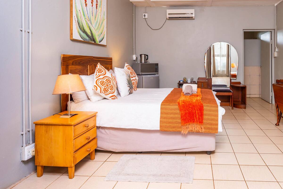 A neatly arranged hotel room with a bed, bedside table, lamp, and a small desk with a chair.