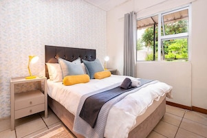Una cama bien tendida con un cabecero, dos mesitas de noche con lámparas y una ventana con cortinas.