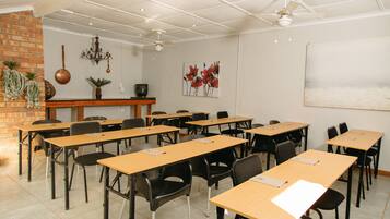 A classroom with wooden desks and black chairs, a brick wall, a chandelier, and a painting on the wall.