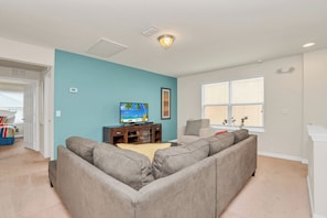 A living room with a large gray sectional sofa, a television on a wooden stand, and a window with blinds. - South-Facing Pool • Conservation View • Game Room • No Rear Neighbors • Disney (Davenport)