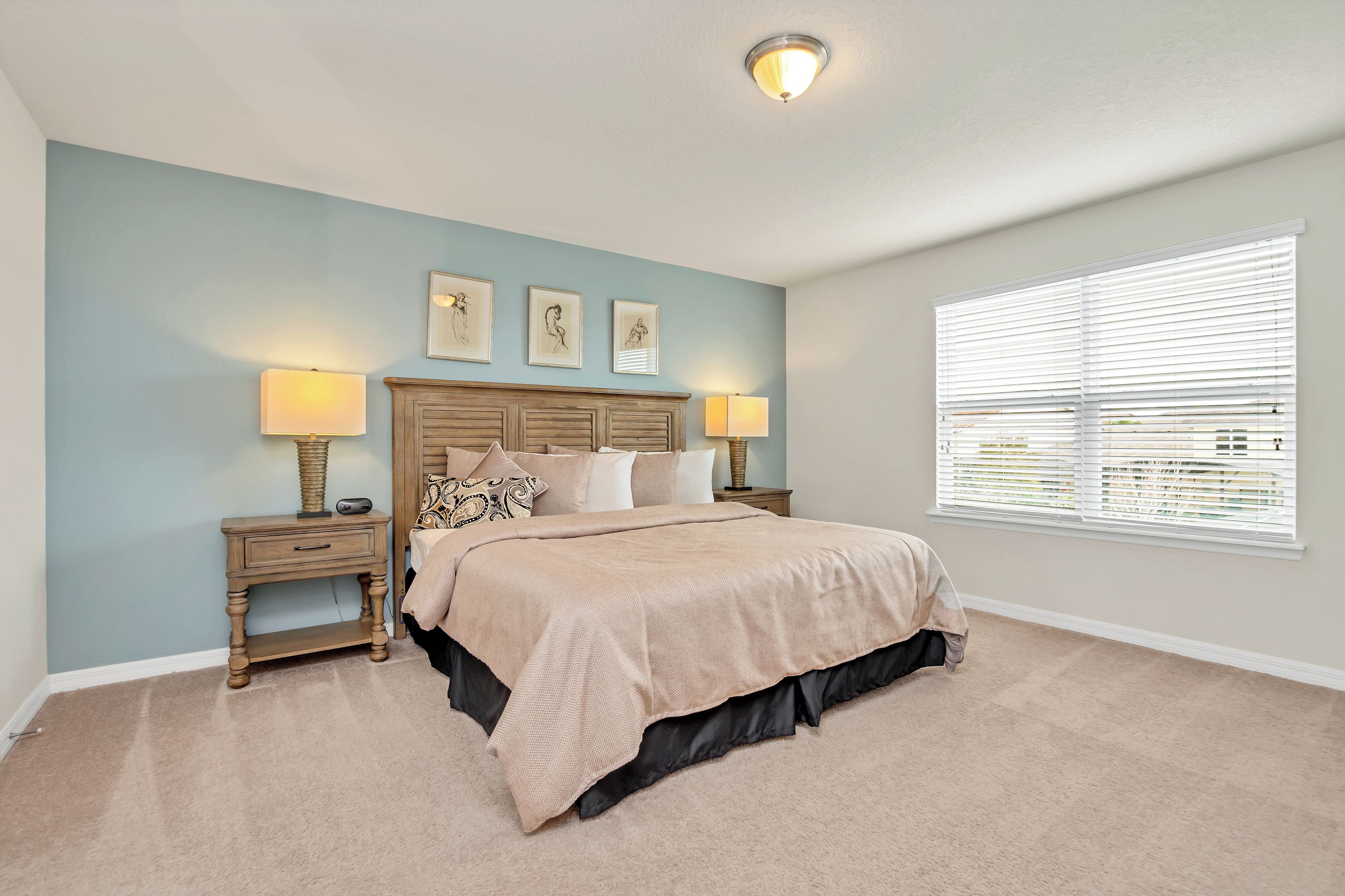 A bedroom with a bed, two bedside tables with lamps, a headboard, and a window with blinds.