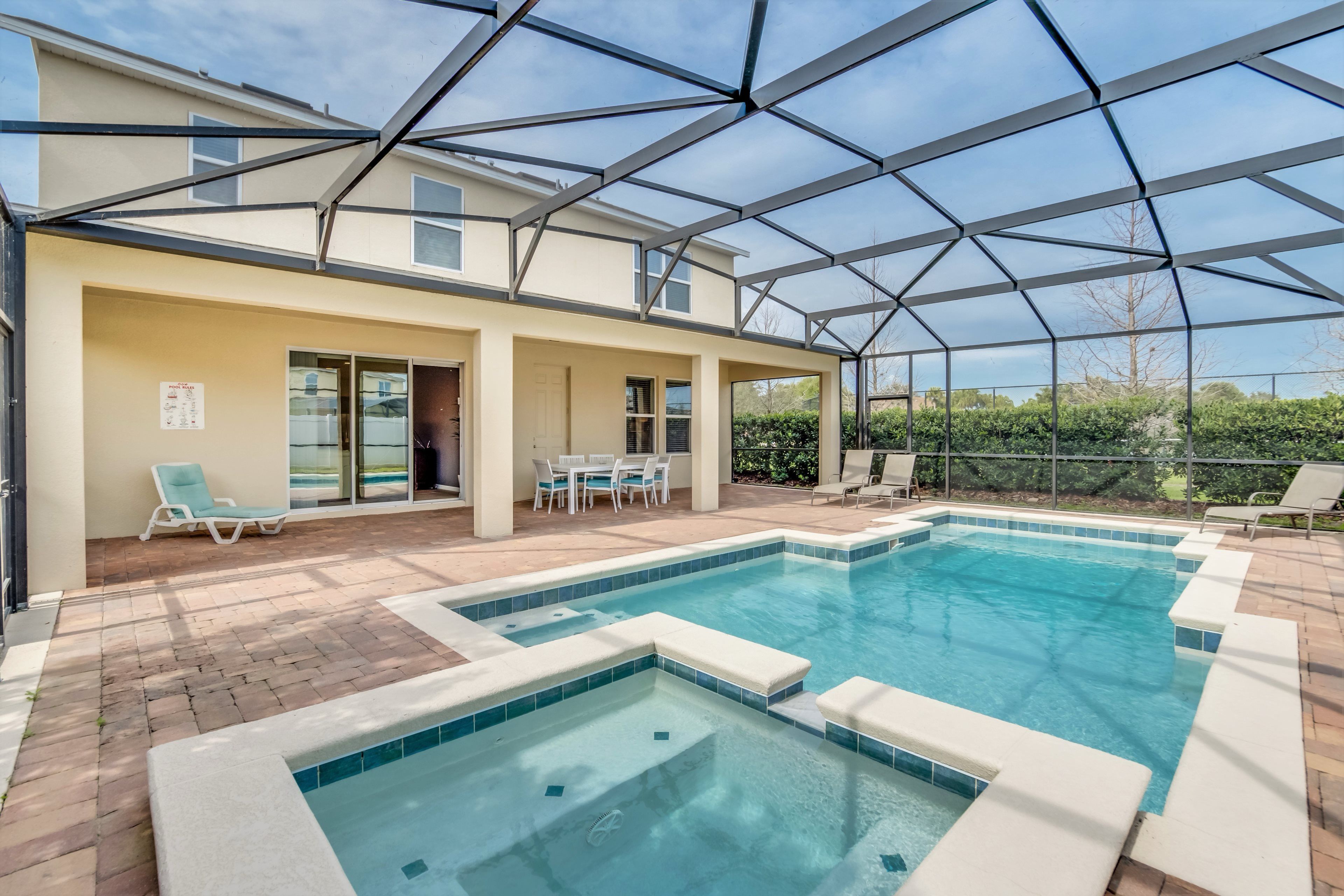 Una piscina exterior cubierta con zona de patio, sillones de descanso y una mesa.