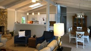 A spacious living area with a fireplace, a dining table with chairs, and a kitchen in the background. - Just One More Day: 2 Kayaks, Wifi, Horseshoes, Paddleboard, Panoramic View (Huddleston)