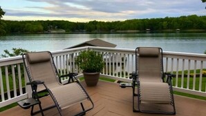 A deck with two lounge chairs and a potted plant, overlooking a lake with a forested shoreline. - Just One More Day: 2 Kayaks, Wifi, Horseshoes, Paddleboard, Panoramic View (Huddleston)