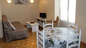 A cozy room with a bed, a small table, a TV, and a dining table with chairs. - Bright T2 Apartment in La Roche-Posay Center with Wi-Fi and Washer (La Roche-Posay)