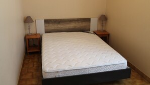 A small, neatly made bed with a wooden headboard and two bedside tables, each with a lamp. - Bright T2 Apartment in La Roche-Posay Center with Wi-Fi and Washer (La Roche-Posay)