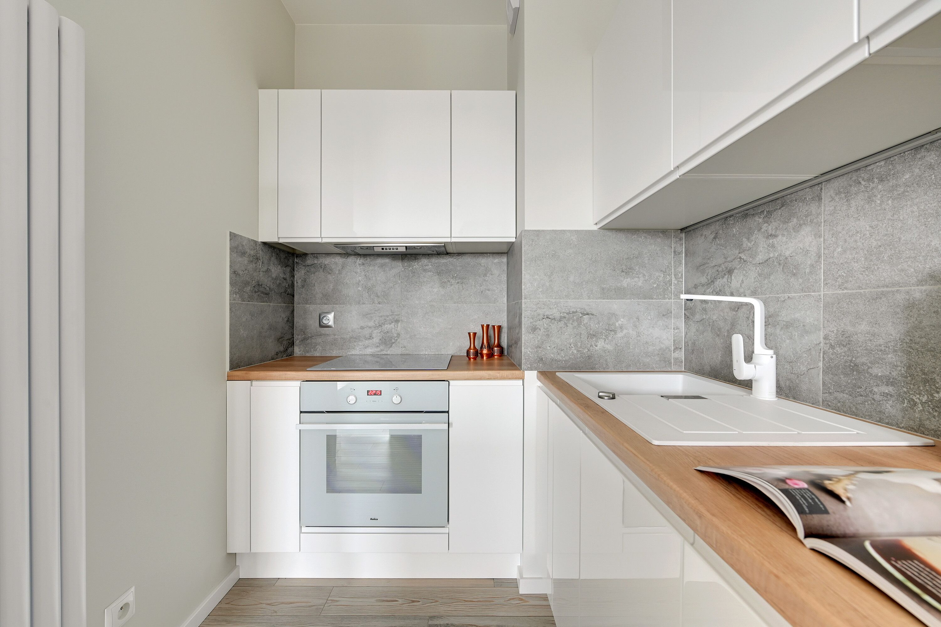 Een kleine keuken met witte kasten, een ingebouwde oven, een spoelbak en een houten aanrecht.