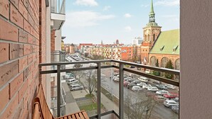A view from a balcony overlooking a parking lot and a cityscape with historic buildings and a church spire. - Flats For Rent - Garden Gates (Gdansk)