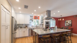 A modern kitchen with white cabinets, stainless steel appliances, a large island with bar stools, and a red accent wall. - The Ranch - Private Pool / Games / Outdoor Fire pit- 3BD / Huge Office (Phoenix)