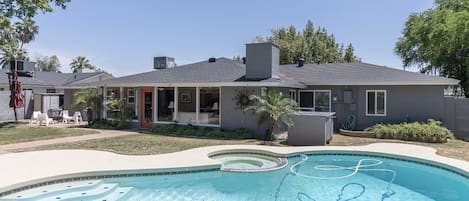 A residential house with a swimming pool, a covered patio, and a lawn.