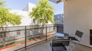 Un balcón con una mesa y sillas, con vista a una calle arbolada y edificios.