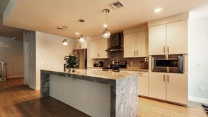 Una cocina moderna con una isla central, electrodomésticos de acero inoxidable e iluminación colgante.