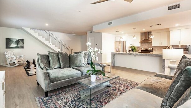 Una sala de estar moderna con un sofá gris, una mesa de centro de vidrio y una escalera que conduce a un piso superior.