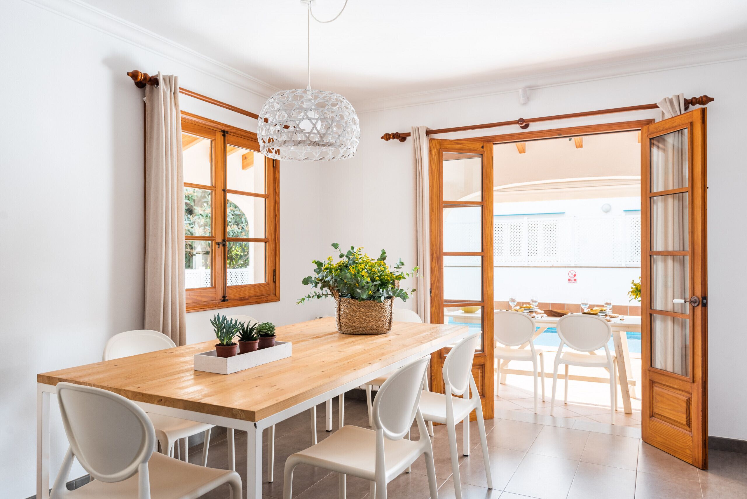 Un comedor con mesa de madera, sillas blancas y lámpara colgante.