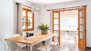 Un comedor con mesa de madera, sillas blancas y lámpara colgante.