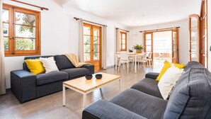 Una sala moderna con un sofá gris, una mesa de centro de madera y una zona de comedor con una mesa y sillas blancas.