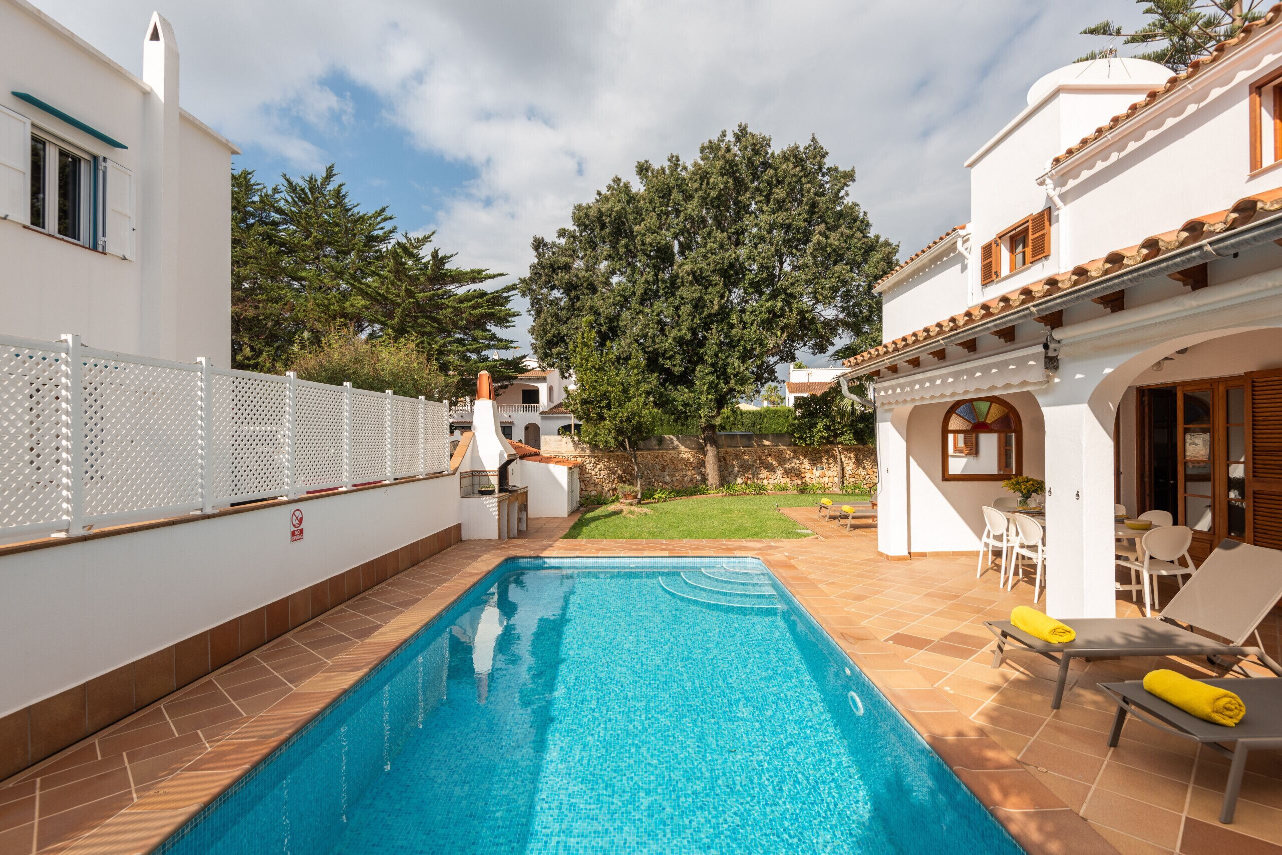 A swimming pool with a tiled deck, a fenced area, and a patio with outdoor furniture.