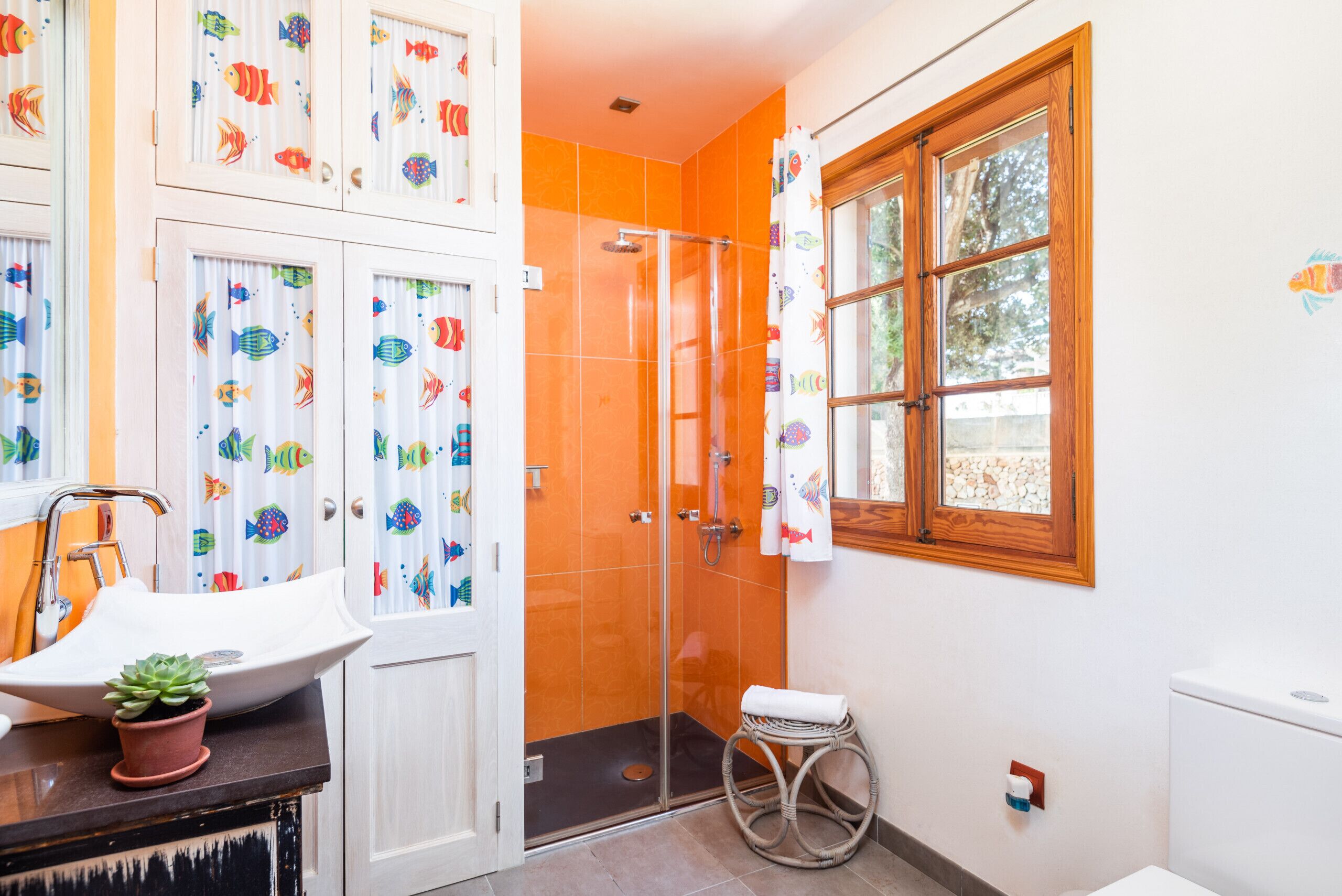 A bathroom with a white sink, a shower with orange tiles, and a window with a wooden frame.