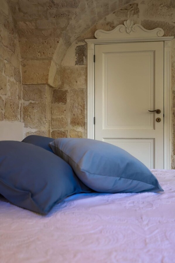A bedroom with a stone wall, a white door, and two pillows on the bed.