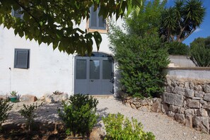 A building with a white facade, a grey door, and a stone wall. - Ostuni Blue Room Suite                                       (Ostuni)