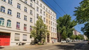 Straßenansicht mit mehrstöckigen Gebäuden, einer roten Tür und geparkten Fahrzeugen.