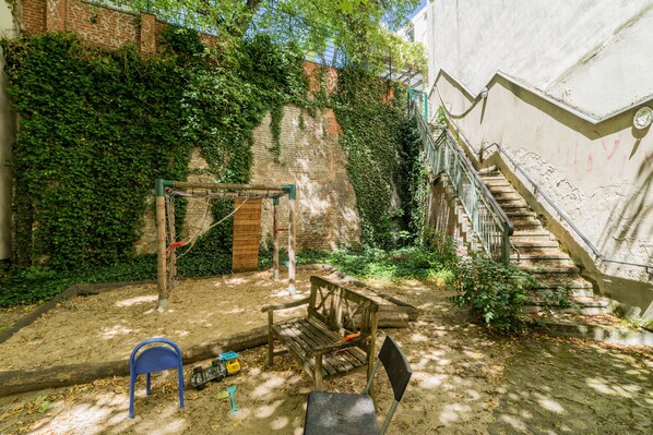 A courtyard with a wooden bench, a blue chair, and a swing set. - Studio apartment in Berlin-Mitte (Mitte)