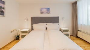 Ein ordentlich bezogenes Bett in einem Hotelzimmer, mit Kopfteil, Nachttischen und einem Beistelltisch.