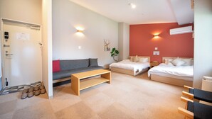 Une chambre d’hôtel moderne avec un canapé, deux lits simples, une table basse en bois et une petite plante.