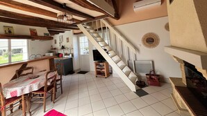 A kitchen with a dining table, chairs, a staircase, and a television. - Charming Cottage 6km from La Roche-Posay - Terrace, Garden, Baby Equipment, Pet Friendly, Wifi (La Roche-Posay)
