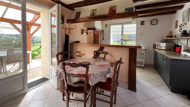 A dining area with a table and chairs, a kitchen counter with appliances, and a view through a glass door. - Charming Cottage 6km from La Roche-Posay - Terrace, Garden, Baby Equipment, Pet Friendly, Wifi (La Roche-Posay)
