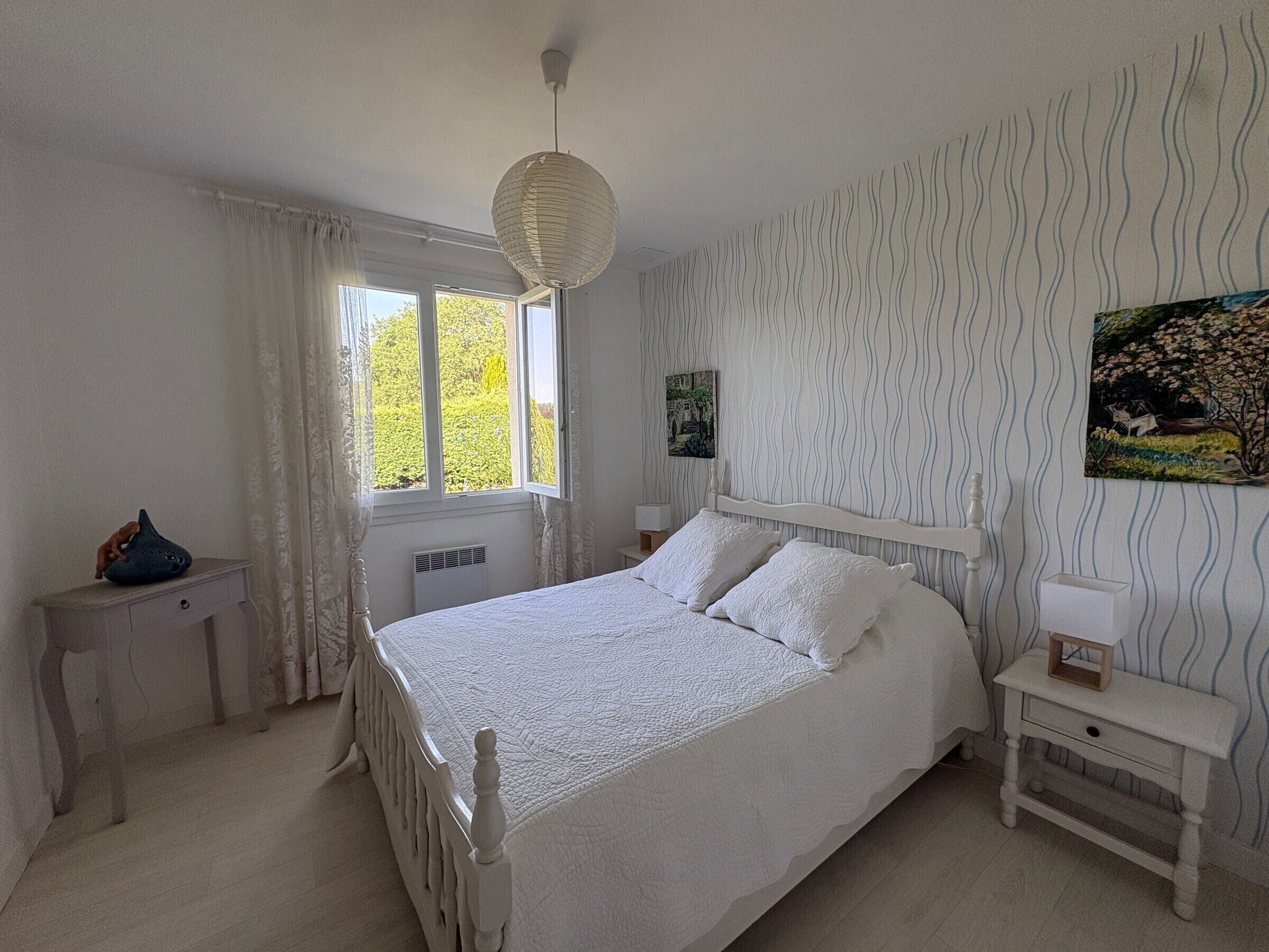 Une chambre à coucher comprenant un lit, une table de chevet, une commode, une fenêtre et un mur orné d’un motif ondulé.