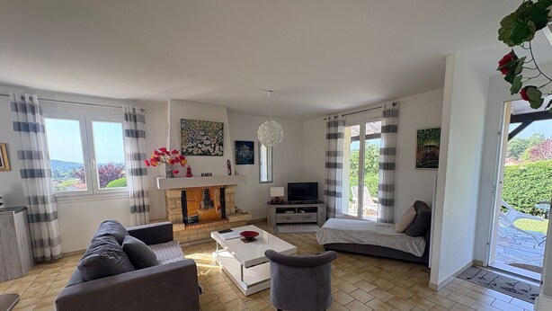 A living room with a sofa, coffee table, fireplace, television, and large windows with curtains. - Cozy House with Garden near Thermes du Connétable - 2 BR, Fully Equipped, WiFi, Sleeps 4 (La Roche-Posay)
